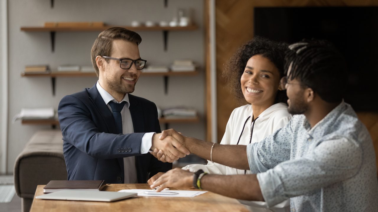Broker shaking hands with a couple across the closing table